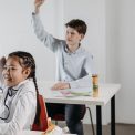 Students actively participating in a classroom setting, seated at desks with raised hands.
