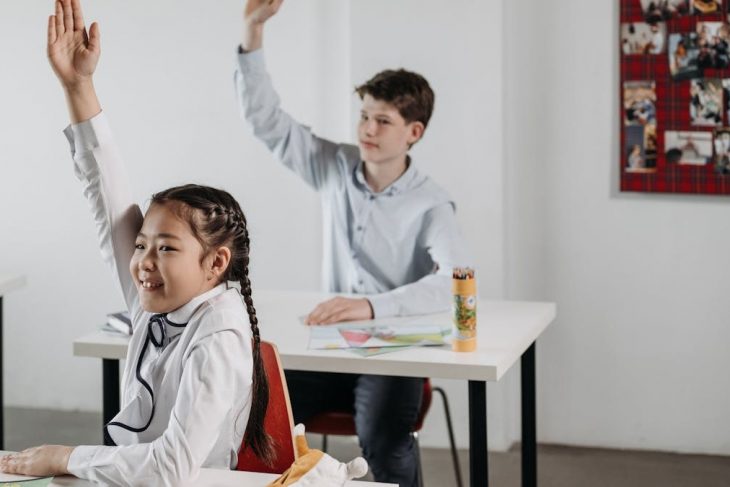 Students actively participating in a classroom setting, seated at desks with raised hands.